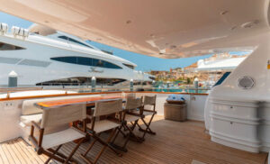 Elegant Outdoor Dining Area on a Luxury Yacht in Cabo San Lucas The outdoor dining area on a luxurious yacht in Cabo San Lucas. A wooden table with seating is placed on the deck, overlooking the marina, with another large yacht visible in the background. The sleek design and spacious surroundings make it an ideal spot for relaxed dining while enjoying the view.
