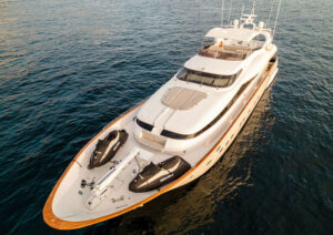 Aerial View of a Luxury Yacht with Jet Skis Aerial shot of an opulent luxury yacht with jet skis on the deck, cruising on the serene waters. The sleek white exterior, paired with its stylish design, reflects the essence of high-end sailing. The yacht is equipped with modern amenities and is perfect for those seeking a luxurious maritime adventure.