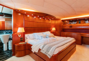 Luxury Yacht Master Bedroom with Elegant Wood Paneling Spacious and luxurious master bedroom aboard a yacht, featuring warm wood paneling, stylish lighting, and plush bedding. The room is equipped with modern amenities, creating a serene and sophisticated atmosphere. The soft lighting enhances the elegance, making it the perfect retreat after a day on the water.