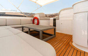 Elegant Lounge Area on a Luxury Yacht's Deck The luxurious lounge area of a yacht featuring comfortable seating, a wooden coffee table, and a scenic view under the sun. The cozy space is perfect for relaxation, surrounded by teak decking and a stylish canopy providing shade for an elegant on-board experience.