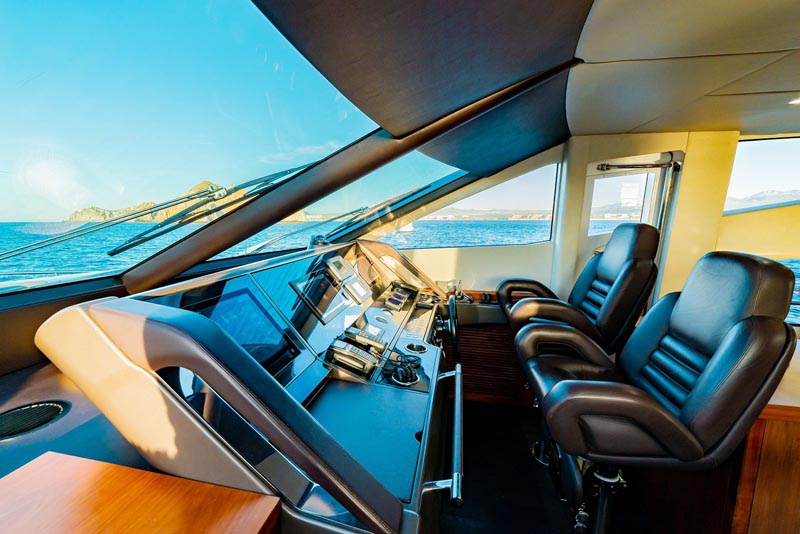 Luxury yacht control room with modern navigation equipment and comfortable captain's chairs, offering a stunning view of the Cabo San Lucas coastline.