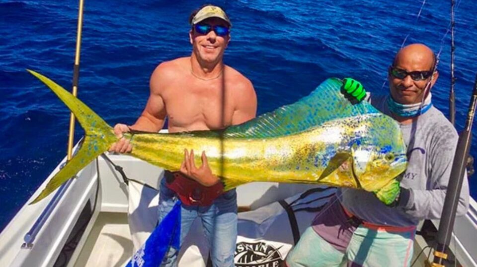 Two men on a boat proudly holding a large golden Mahi Mahi fish, illustrating fishing charters cabo san lucas mexico.