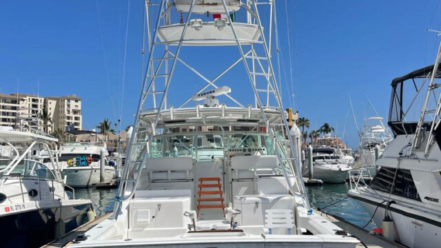 Cabo San Lucas Fishing Charters The "Game On" boat proudly docked in the harbor, showcasing its stunning design and sleek features. The boat’s towering fishing tower is visible, with clear skies and other boats in the background. The name "GAME ON" stands out prominently on the back of the boat, emphasizing its adventurous spirit. The image captures the essence of marine excitement and luxury, offering a view of the boat's expansive deck and its well-maintained exterior.