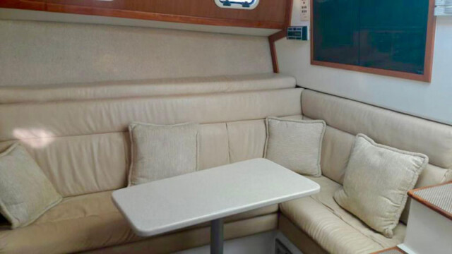 A well-designed, cozy dining nook on the "Game On" boat, featuring a round table surrounded by plush cream-colored cushions. The space offers a comfortable seating arrangement, ideal for enjoying meals or socializing while onboard. A large window allows natural light to filter through, enhancing the bright and airy atmosphere of the cabin. The modern design and thoughtful layout ensure a relaxing experience for guests while at sea.
